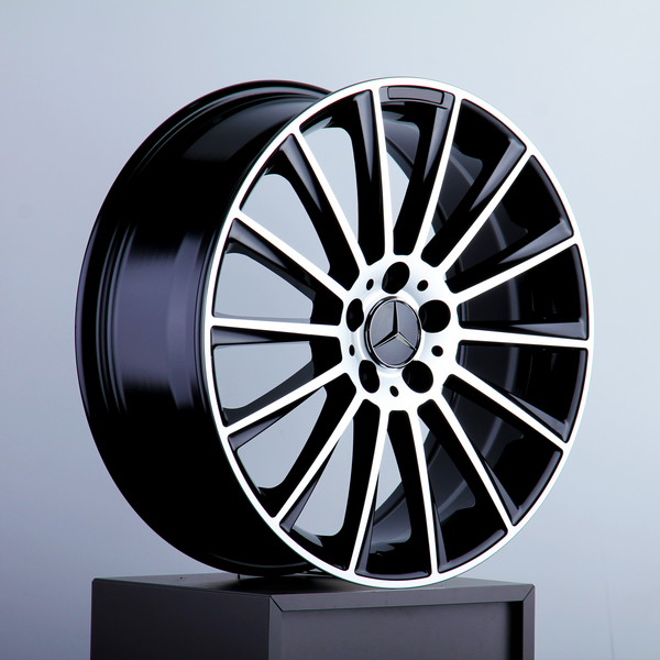 A glossy black and silver alloy wheel with a star emblem rests on a pedestal, set against a plain light gray background.