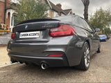 A gray BMW M235i parked on a residential street, showcasing dual exhausts and a rear spoiler. The license plate reads 