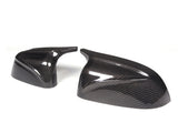 Two carbon fiber side mirror caps, resting on a white background, display a glossy, textured surface with reflective highlights, suggesting a sleek automotive accessory design.