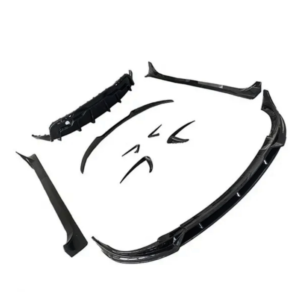 Several black car body kit components are spread out, including a front splitter, side skirts, and bumper lip, arranged on a plain white background.