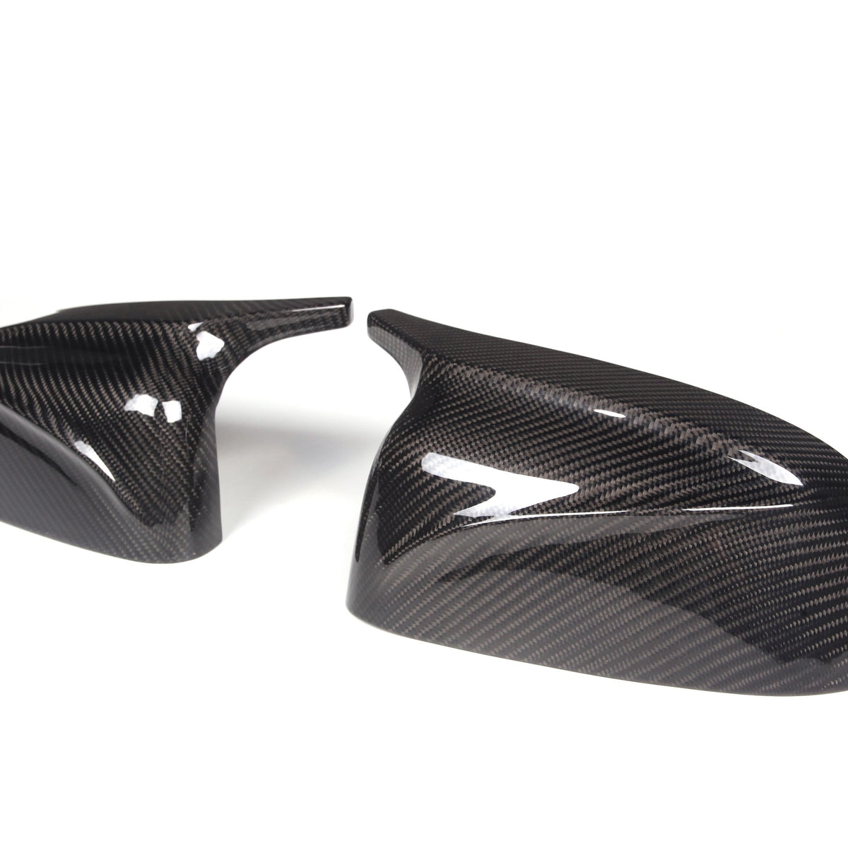 Two carbon fiber mirror covers, glossy with a black and gray weave pattern, are positioned against a plain white background. They exhibit a sleek, aerodynamic design.