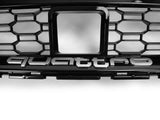 A black car grille with a hexagonal pattern displays the word 