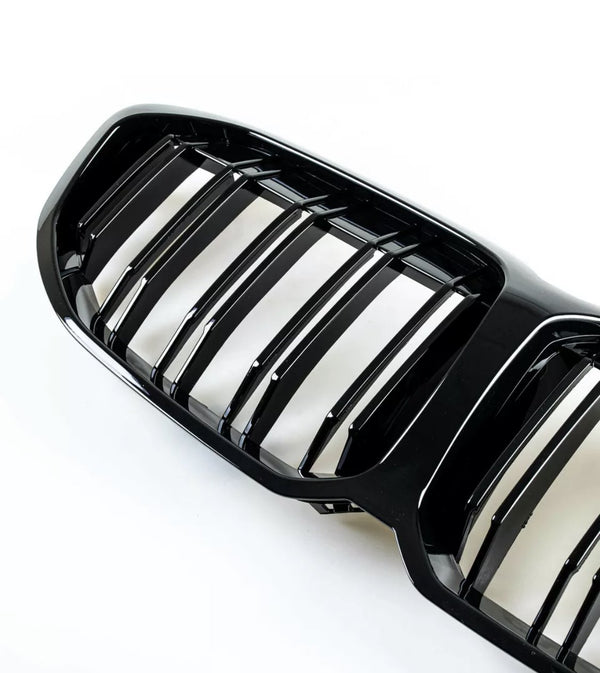 Black car grille with vertical bars, reflecting light. It rests on a plain white background, highlighting the glossy finish and sleek design.