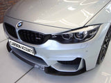 A silver BMW M3 car is parked indoors, showcasing its front grille and headlights. The number plate reads 