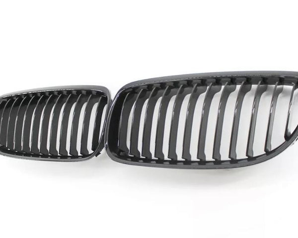 Two black car grille inserts with vertical slats lie side by side on a white background, resembling classic automotive front grille designs.