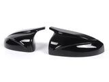 Two glossy black car mirror covers rest side by side, featuring sleek aerodynamic designs, set against a plain white background.