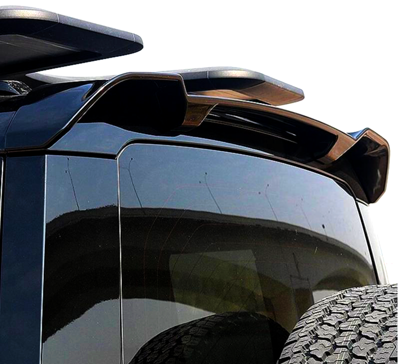 A vehicle's rear window features a sleek, aerodynamic roof spoiler. The scene is bright, and a tire's tread is visible in the lower foreground, suggesting an off-road setting.