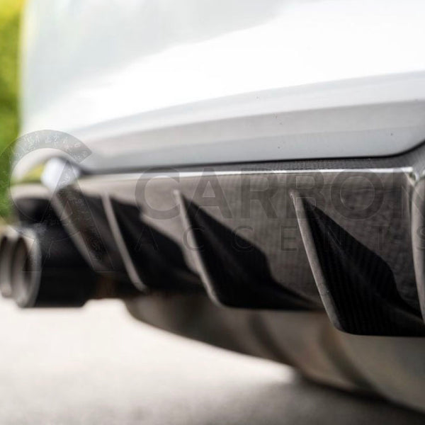 Car rear diffuser with exhaust pipes, surrounded by blurred greenery and pavement. Text reads: "CARBON ACCENTS," faintly visible over the image in gray.