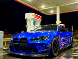 A blue sports car is parked at a gas station with a Shell V-Power Nitro+ pump, under bright canopy lights, reflecting on the wet pavement at night.
