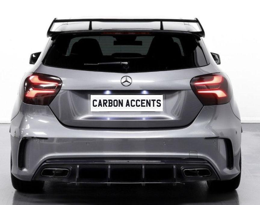 A silver car is parked in a well-lit, indoor space. It displays a license plate with the text "CARBON ACCENTS" and has a prominent rear spoiler and sleek taillights.