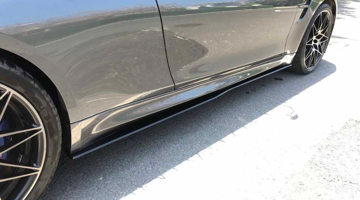 A sleek, dark-colored car is parked on a sunlit street, showcasing its shiny surface and stylish, multi-spoke alloy wheels, with a reflection visible on the vehicle’s side panel.