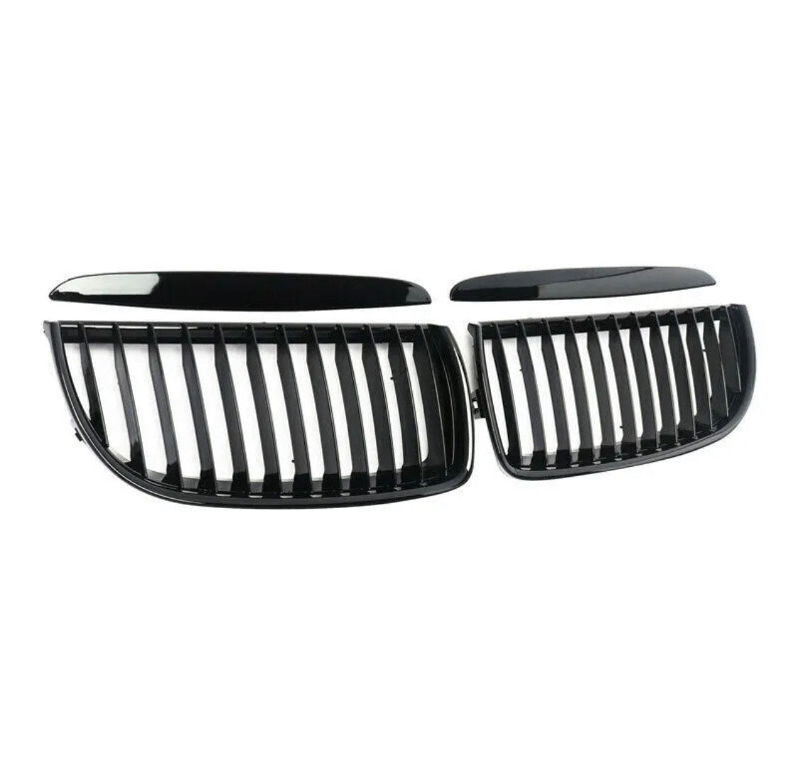 Two black, glossy, kidney-shaped car grilles with vertical slats are lying on a white background, separated into two symmetrical sections.