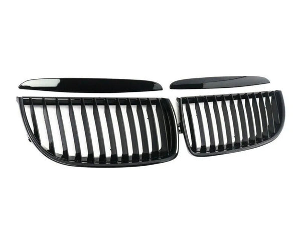 Two black, glossy, kidney-shaped car grilles with vertical slats are lying on a white background, separated into two symmetrical sections.