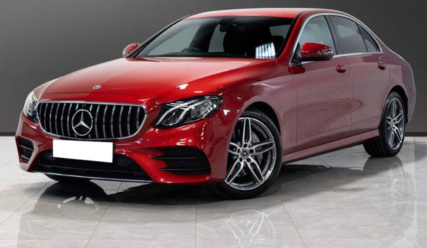 A red Mercedes-Benz sedan is parked on a reflective tiled floor, with a gray gradient background. The car's design features prominent silver rims and a front grille with the iconic emblem.