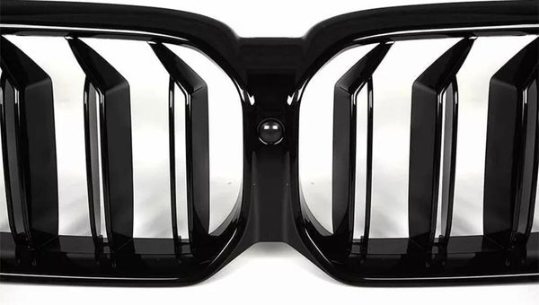 Black car grille with vertical slats is centered with a circular camera. It is positioned against a clean, white background, emphasizing its sleek, modern design.