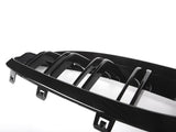 A glossy black car grille with vertical slats rests against a bright white background, featuring attachment clips at the bottom edge.