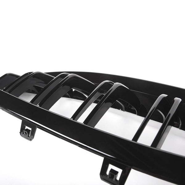 A glossy black car grille with vertical slats rests against a bright white background, featuring attachment clips at the bottom edge.