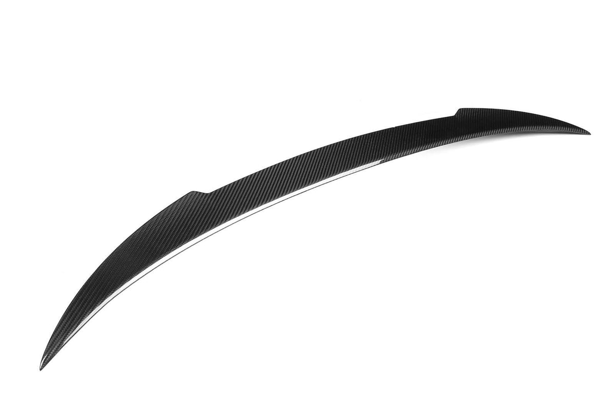 A curved, carbon-fiber car spoiler is shown in close-up, lying flat against a plain white background. It has a sleek, aerodynamic design with a textured surface.
