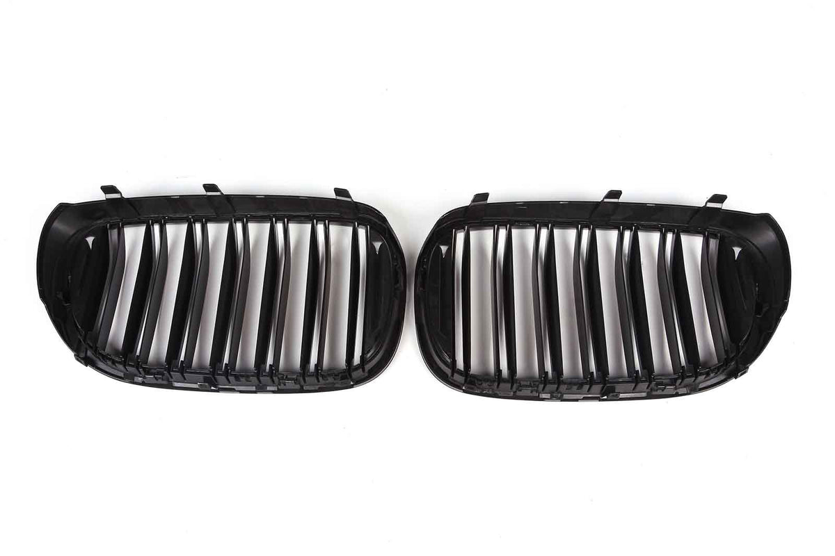 Two black car grille inserts rest on a white background, featuring vertical slats and curved edges, designed to fit the front of a vehicle.