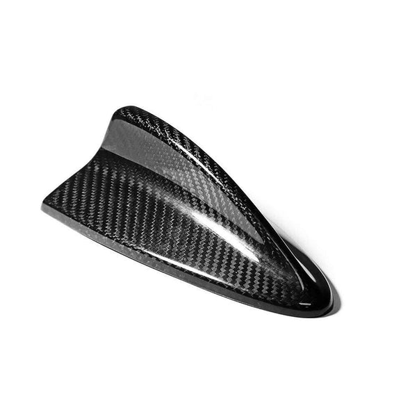 A black carbon fiber shark fin-shaped antenna is resting on a plain white background, highlighting its sleek, glossy texture and aerodynamic design.