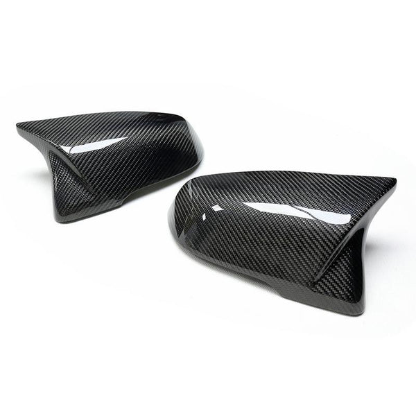 Carbon fiber mirror caps rest side by side on a white surface, displaying their glossy, textured design typically used for automotive exterior upgrades.