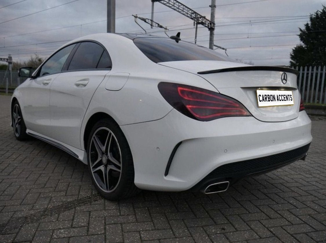 A white car is parked on a paved area near railway wires. The license plate reads "CARBON ACCENTS," and the car features sleek tail lights and shiny wheels.