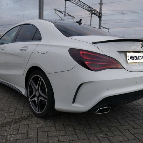 A white car is parked on a paved area near railway wires. The license plate reads "CARBON ACCENTS," and the car features sleek tail lights and shiny wheels.