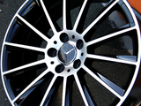 A sleek, black and silver alloy wheel with a prominent star emblem is resting on a textured, gray surface.