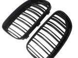 Two black car grille inserts, featuring vertical slats, lie angled against a white background. They are separated, showing both the front and back view of each grille.