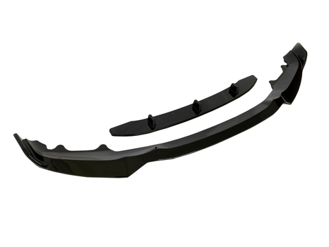 A black car front lip spoiler kit lies on a white background. The main curved piece is accompanied by a smaller, straight piece with three fins, designed for vehicle aerodynamics.