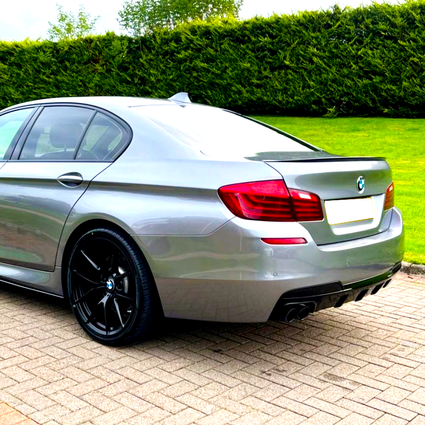 A silver sedan with a sleek design is parked on a paved driveway, surrounded by neatly trimmed grass and tall hedges.