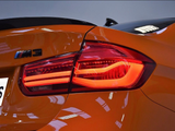 A close-up of an orange car's rear, displaying its lit brake light and an 