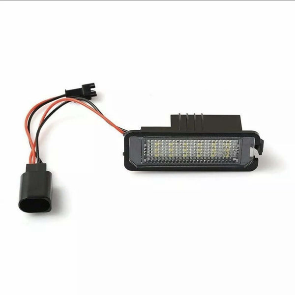 An LED light fixture with a rectangular design and grid pattern surface is connected to two red and black wires, lying against a plain white background.