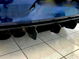 Four black exhaust pipes are protruding from the rear of a blue car, positioned over glossy tiled flooring in an indoor showroom setting.