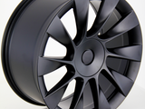 A matte black alloy wheel with multiple spokes is positioned upright. It rests on a clean, white surface, showcasing its sleek, modern design against a plain background.
