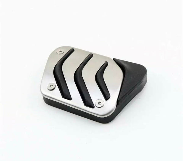 A rectangular metal pedal cover features three raised black rubber strips, bolted onto a black plastic base, resting on a plain white background.