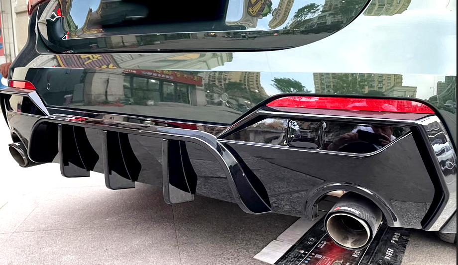 A car's rear features a sporty diffuser and dual exhaust pipes, parked on an urban street with reflections of nearby buildings on its glossy black surface.