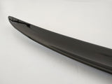 Shiny black car spoiler, curving slightly upward, sits on a smooth, light gray surface.