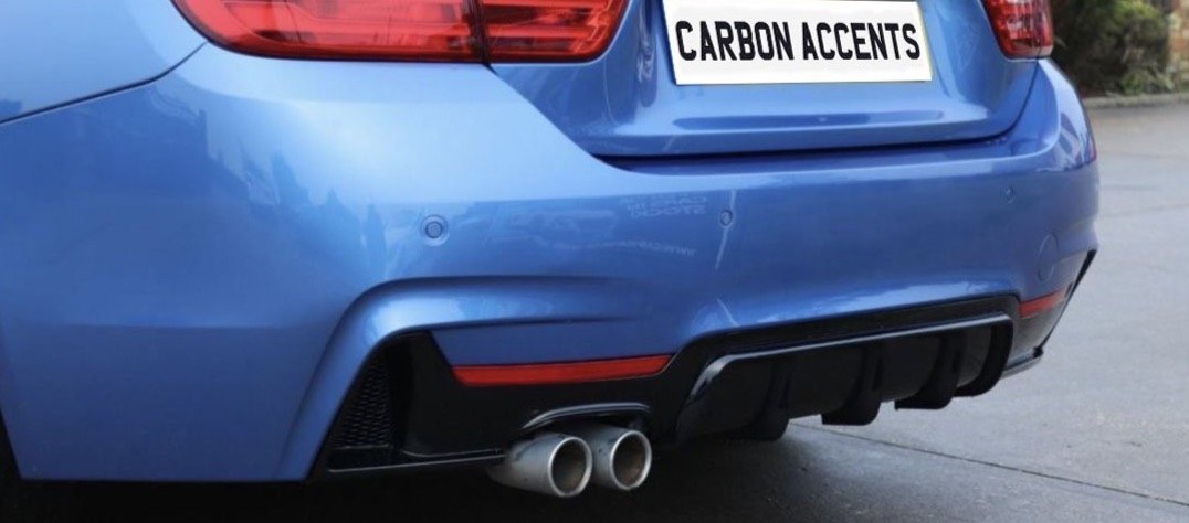 A blue car's rear with dual exhaust pipes; above them, a white license plate reads "CARBON ACCENTS." The scene is set in a paved outdoor area.
