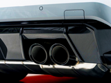 Twin exhaust pipes protruding from a vehicle's rear bumper with carbon fiber detailing, against a blurred background, highlighting the car's sporty design.