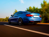 A blue sports car speeds along a two-lane highway with trees blurred in the background, under a clear blue sky with a few clouds.