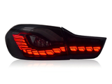 A sleek car taillight is illuminated with vibrant red LED segments, arranged in a distinctive, angular pattern. It is set against a plain, white background.