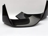 Two carbon fiber car parts, possibly rear exhaust diffusers, are positioned diagonally on a solid white surface, highlighting their glossy black finish and textured pattern.