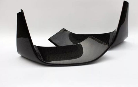 Two carbon fiber car parts, possibly rear exhaust diffusers, are positioned diagonally on a solid white surface, highlighting their glossy black finish and textured pattern.