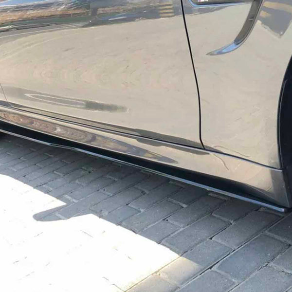 A sleek car with glossy dark wheels is parked, reflecting sunlight on its shiny surface, situated on a paved area.