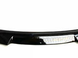 A black car spoiler with a glossy finish is positioned horizontally on a plain white background. The design is sleek, slightly curved, and features a central reflective strip.