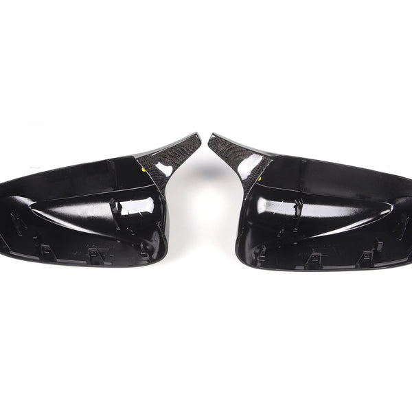 Two black, glossy car side mirror covers face each other, highlighting their contoured interior and carbon fiber textures, set against a plain white background.