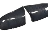 Two carbon fiber mirror covers rest side by side, reflecting light on their glossy surface, set against a plain white background.