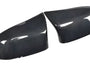 Two carbon fiber mirror covers rest side by side, reflecting light on their glossy surface, set against a plain white background.