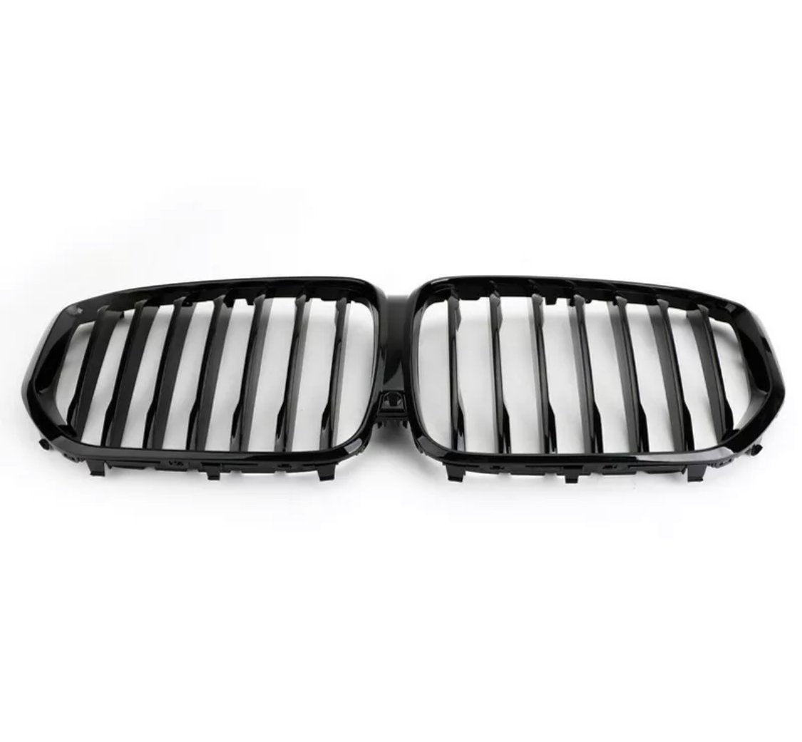 A black, dual kidney-shaped car grille features vertical slats, designed for a vehicle's front end. It rests against a plain white background, emphasizing its sleek design.